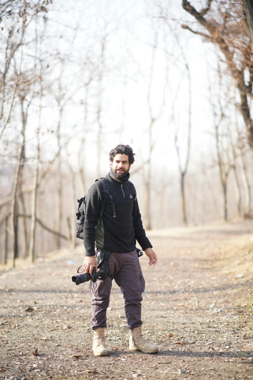 man holding camera in large wooded area with bare trees