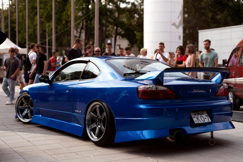 blue sports car parked in front of a crowd on the side of a road