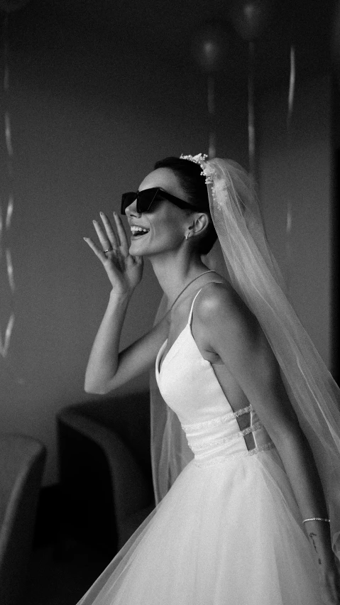 a bride waving and wearing sun glasses with a veil on her head