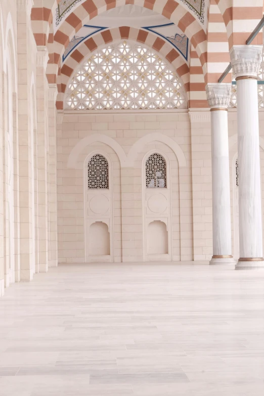 an open room with white and pink walls, arches and windows