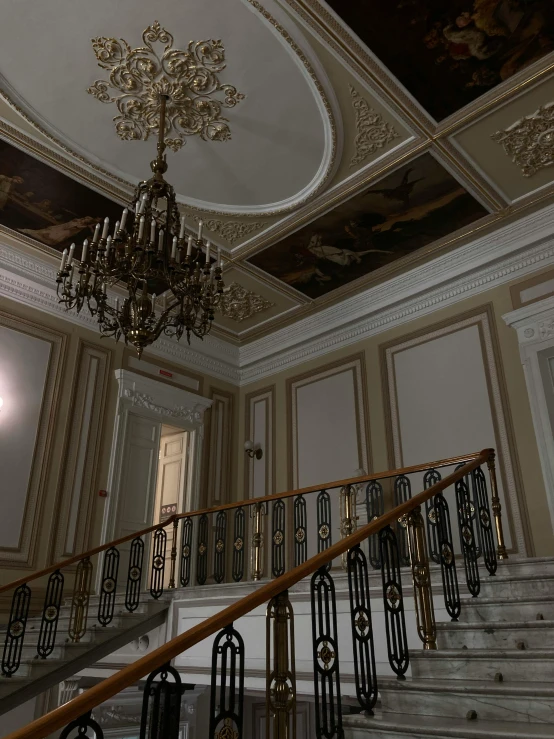 an elegant staircase has gold trim on the walls and is decorated with elaborate ceiling murals