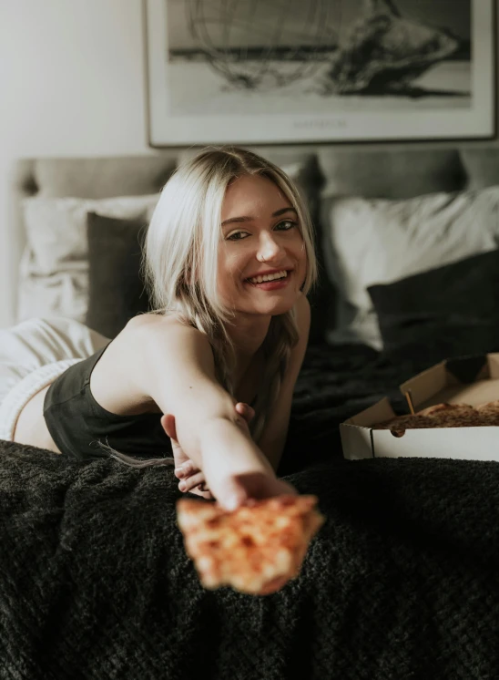 girl laying on a bed holding up a slice of pizza