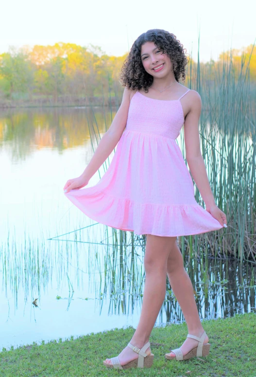 a girl in a pink dress standing on the grass near a lake