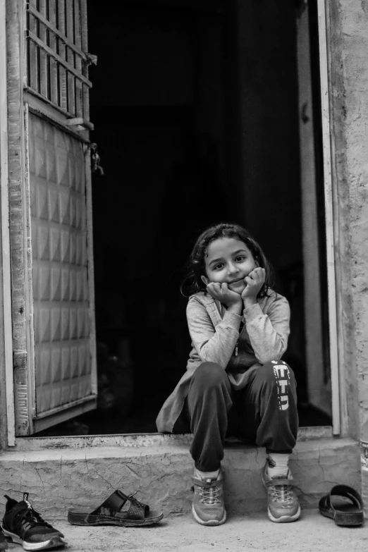 a little girl sits in a doorway and looks sad