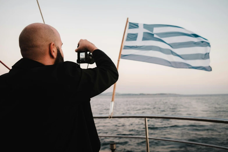 man looking out over water with a greek flag