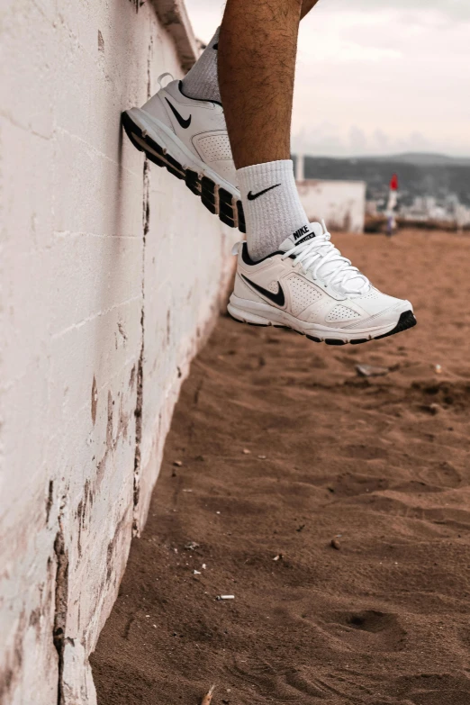 man in white and black sneakers is hanging against a brick wall