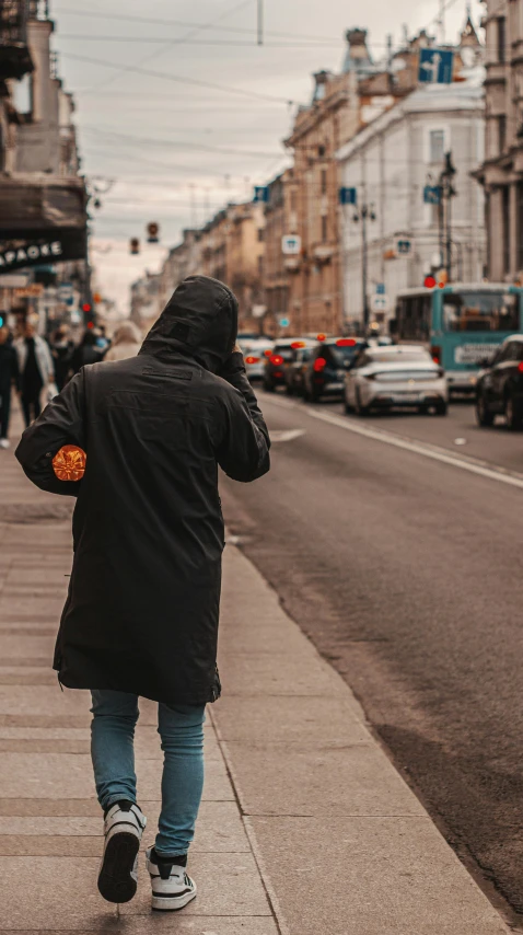 a man in a black jacket and blue jeans is walking on a sidewalk