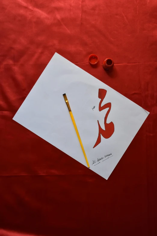 a pencil on top of some red paper next to a drawing with a writing instrument