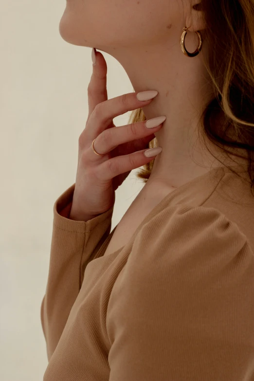 woman in tan sweater and gold rings smoking