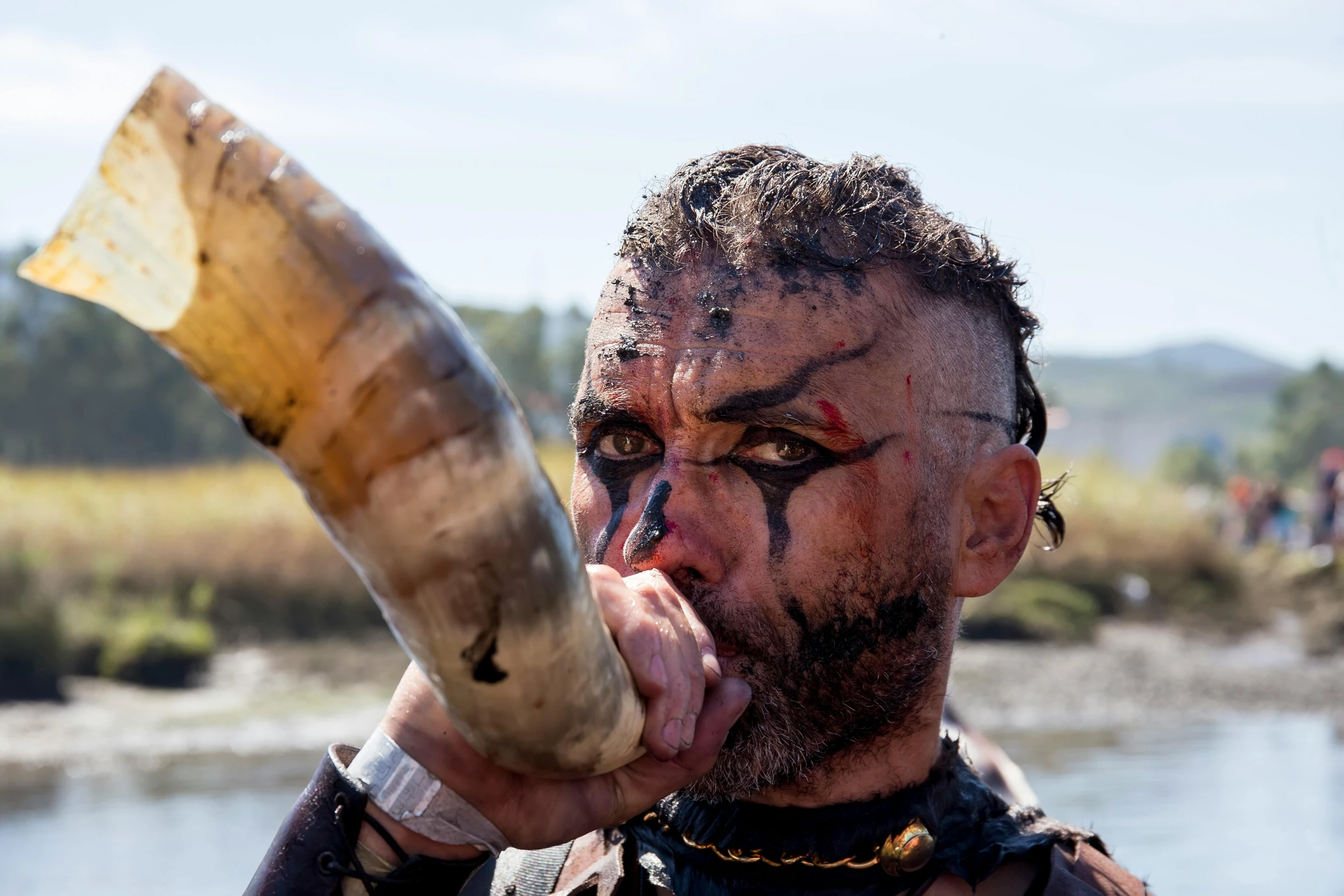 the man with tattoos and makeup is holding a large horn