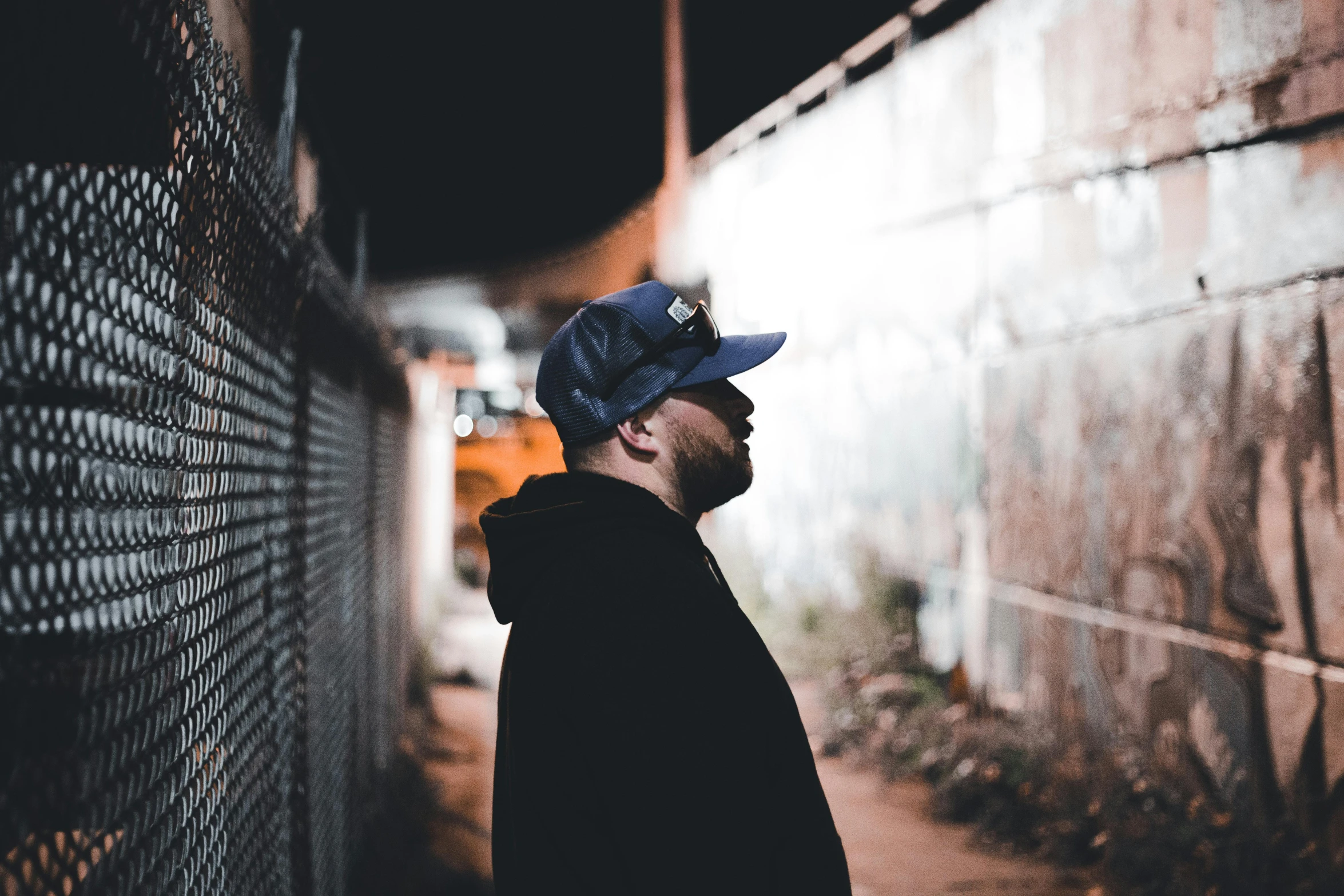 a young man with a cap is standing near a fence