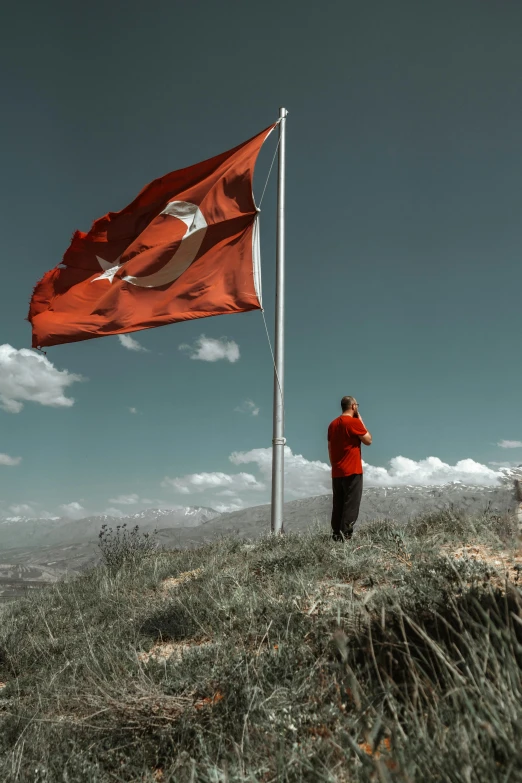 man with a red jacket on taking pictures with his phone near a flag pole