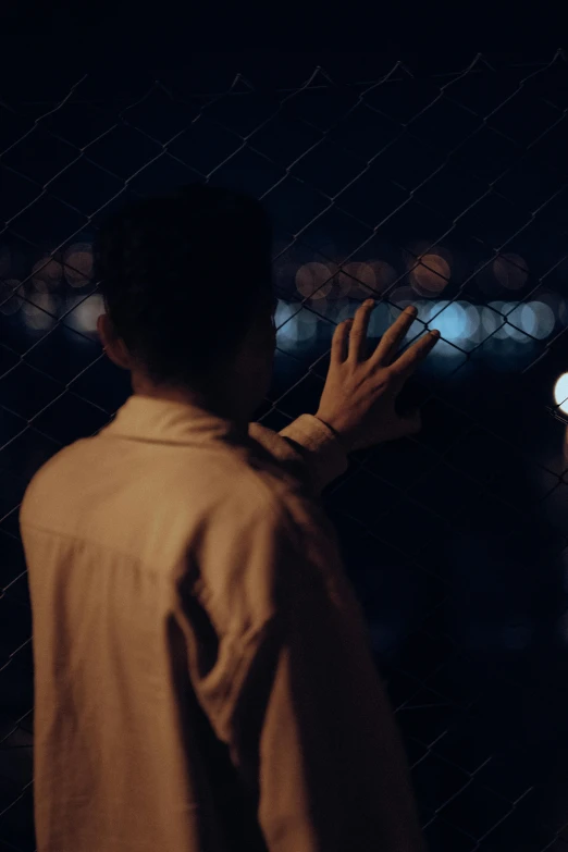 a man holding soing up to his face, standing in front of a chain link fence