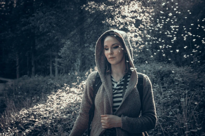 a girl is standing in the forest looking away from the camera