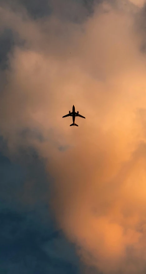 an airplane flying through a cloudy sky in the sunset