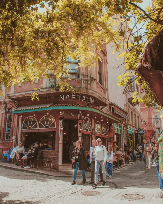 people walking in front of a restaurant with a street sign and trees