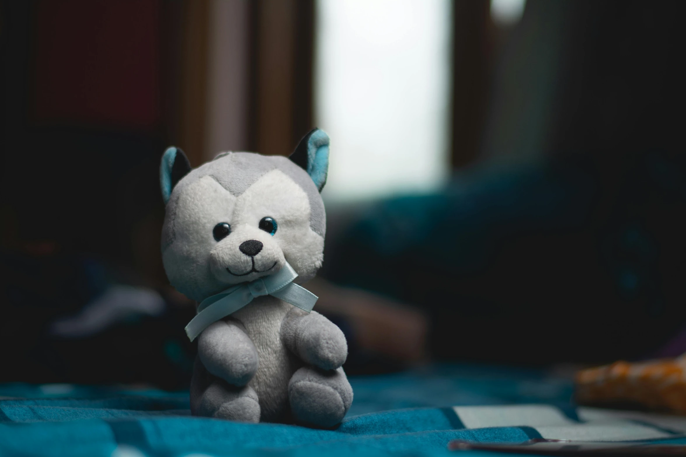 a gray and white teddy bear sitting on a bed