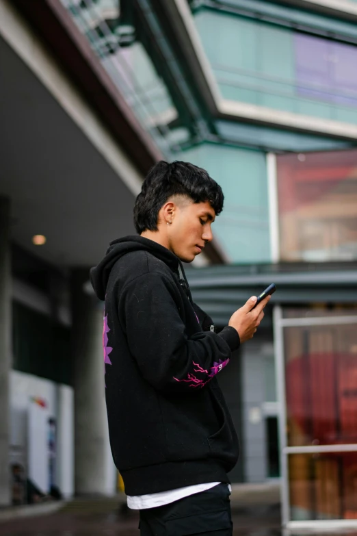 a man wearing a sweatshirt standing in front of a building looking at his phone