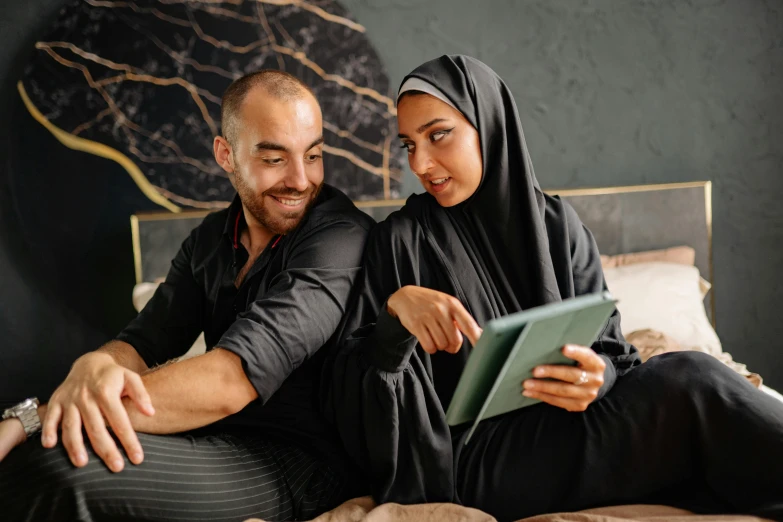 a man and woman sitting on the bed looking at soing