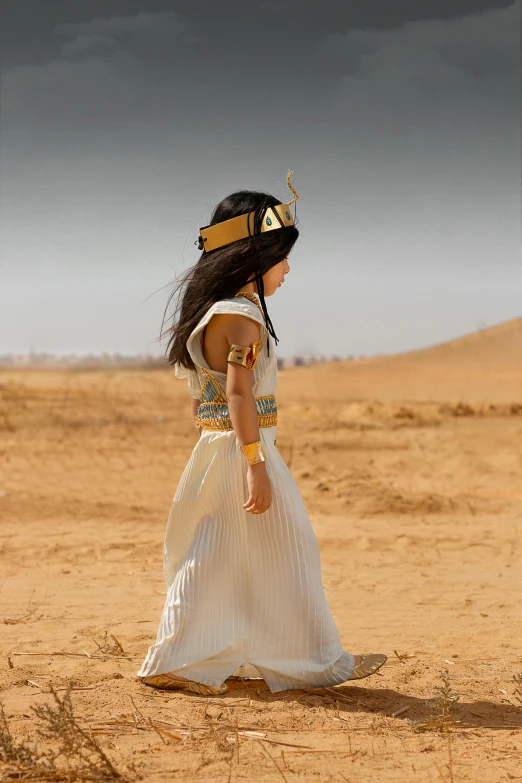 a woman walking through the desert in an egyptian style dress