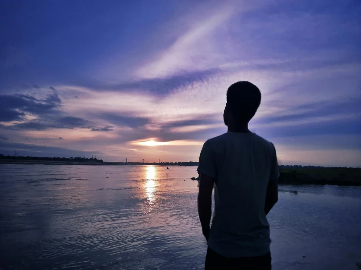 a person standing on the beach near water at sunset