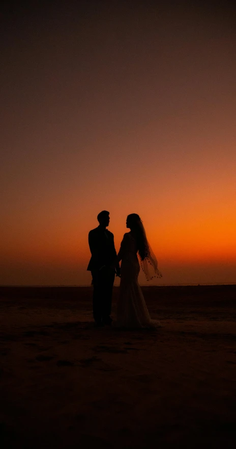 a bride and groom are standing on a beach at sunset