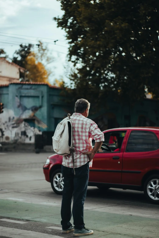 a man with a backpack stands in front of a red car