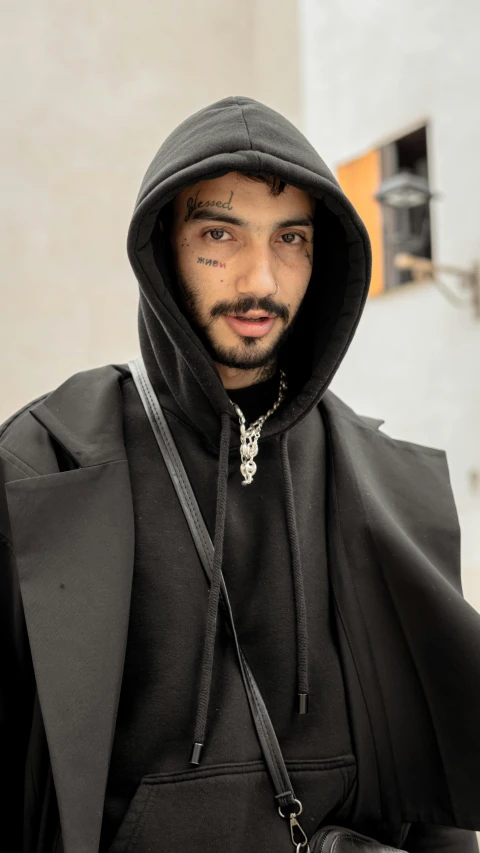 a man with a moustache wearing a black outfit and a hoodie