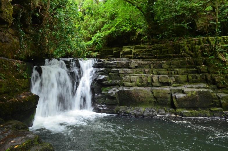 a waterfall surrounded by many large rocks and green trees