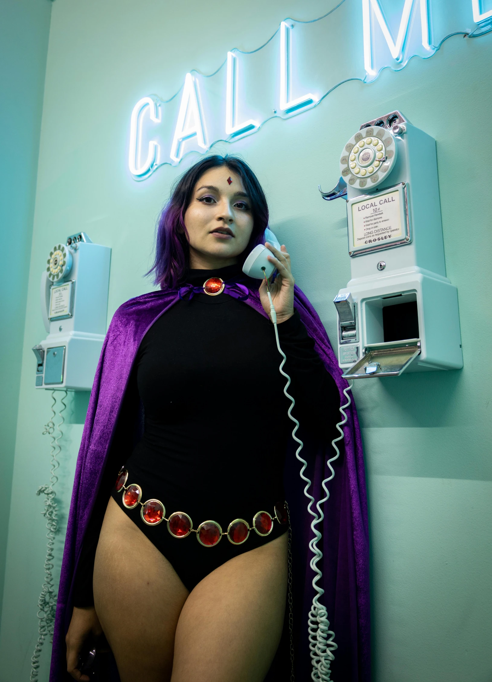 woman in purple cape standing against wall holding phone to her side