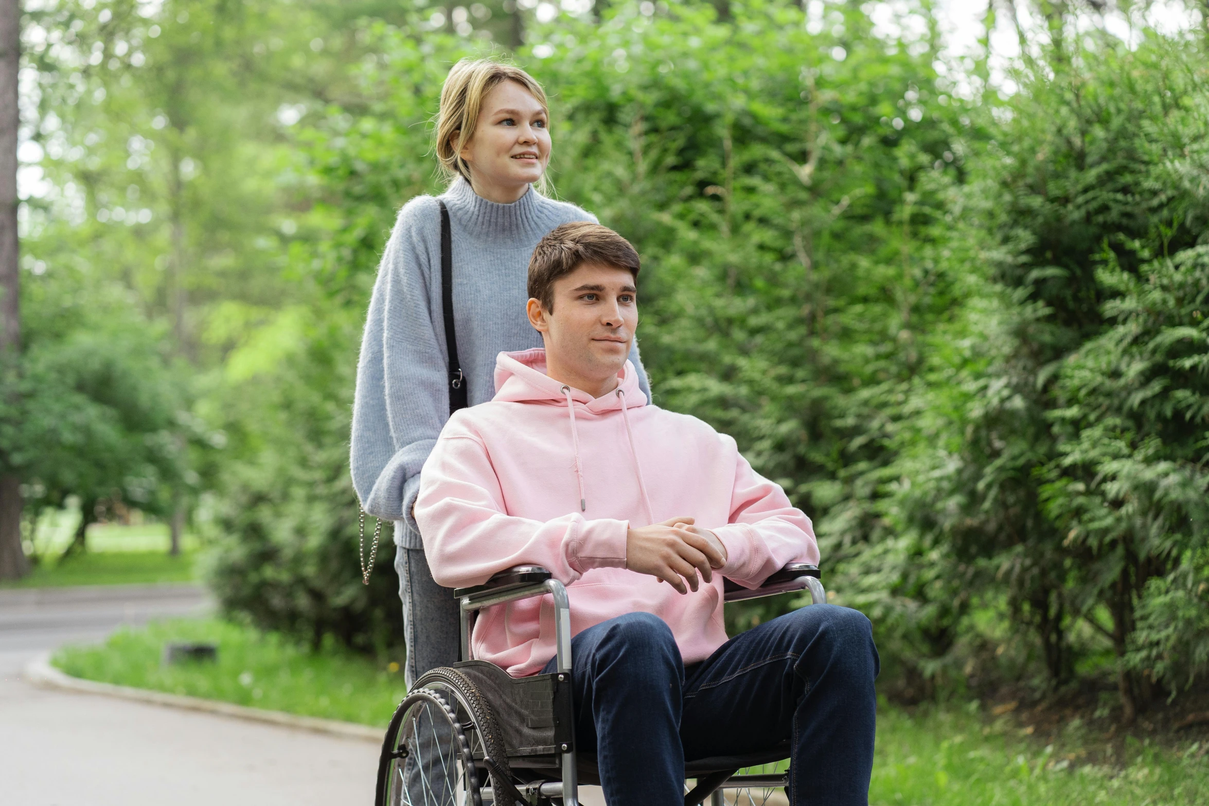 a woman in a pink jacket and a man in a wheelchair are walking through the park