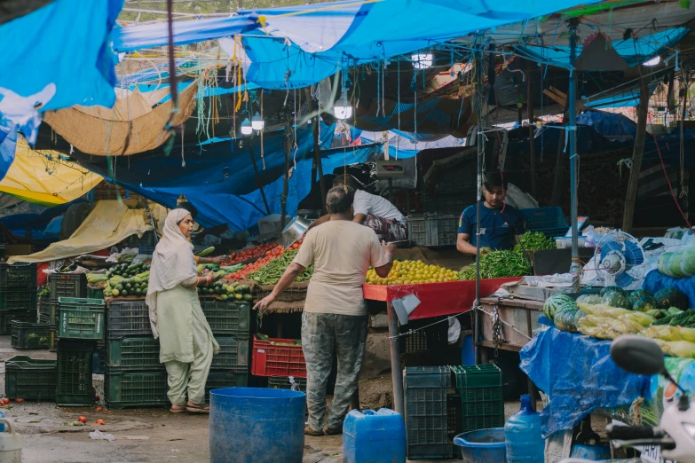 two people walk through an outdoor market where fruit and vegetables are for sale