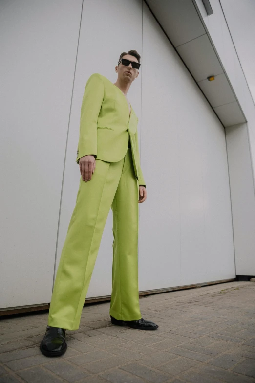 man in green suit posing for po next to wall