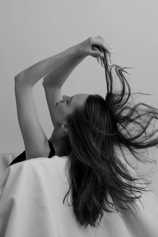 black and white pograph of woman lying in bed with her hair flying