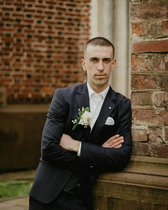 a close - up of a young man standing on a stone wall holding his arms crossed