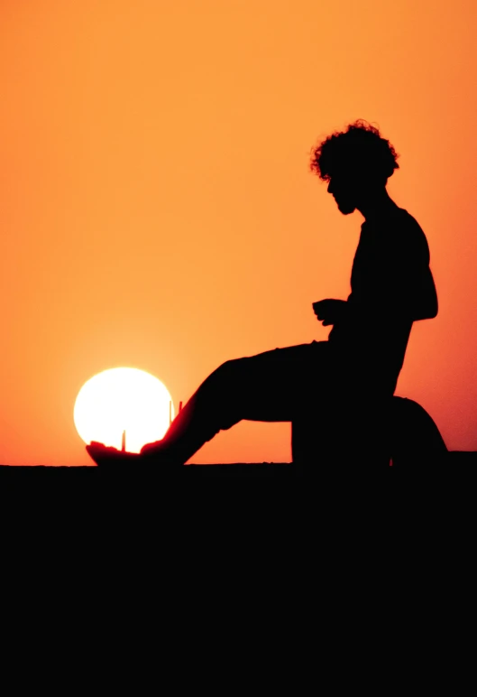 the silhouette of a man sitting on the roof watching the sun set