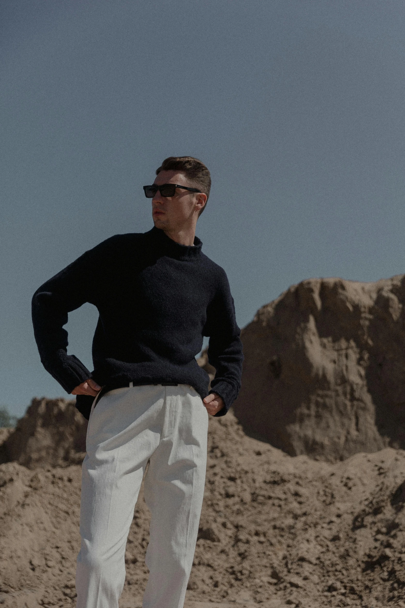 a man stands on top of a mountain while wearing white pants