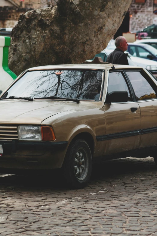 an older brown car parked on a cobblestone road