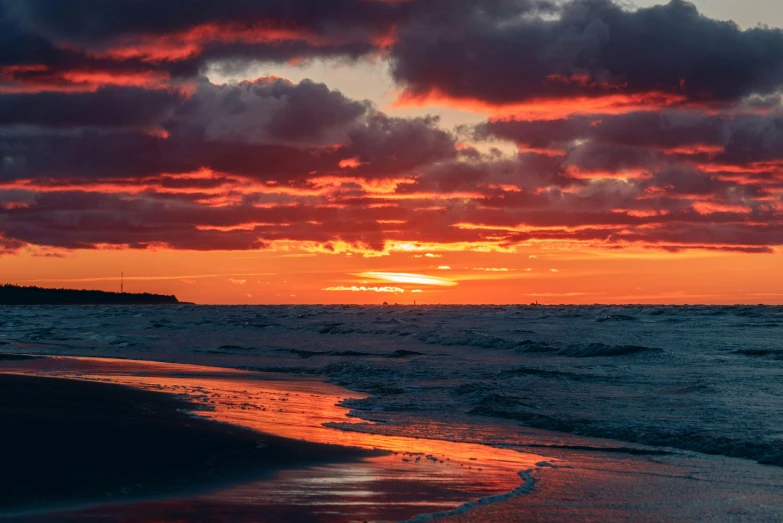 a surfer walking along the ocean with a sunset behind him