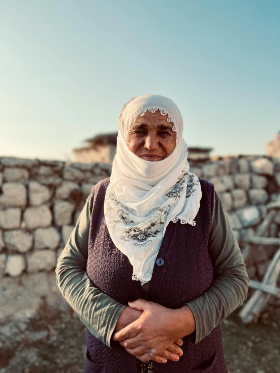 an older woman with a white veil on her head and her hands crossed over her chest, standing outdoors