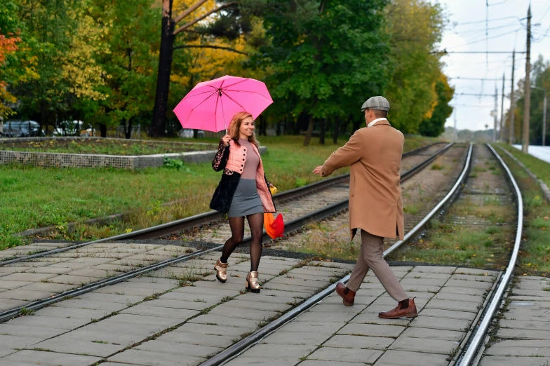 two people walking on the train tracks, one is holding an umbrella