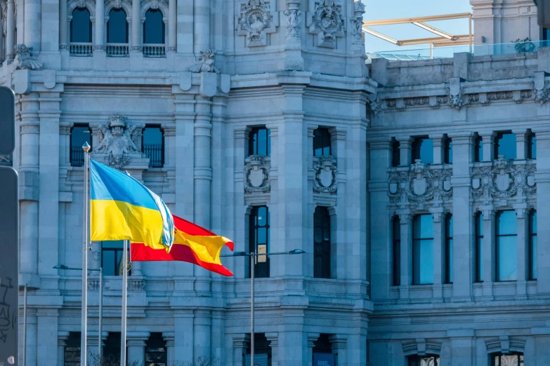 a european and ukraine flag flying on flagspoles near a large white building