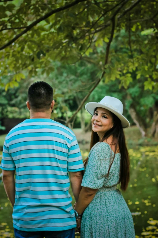 a young woman with long dark hair wearing a hat standing next to a man in blue and green shirt