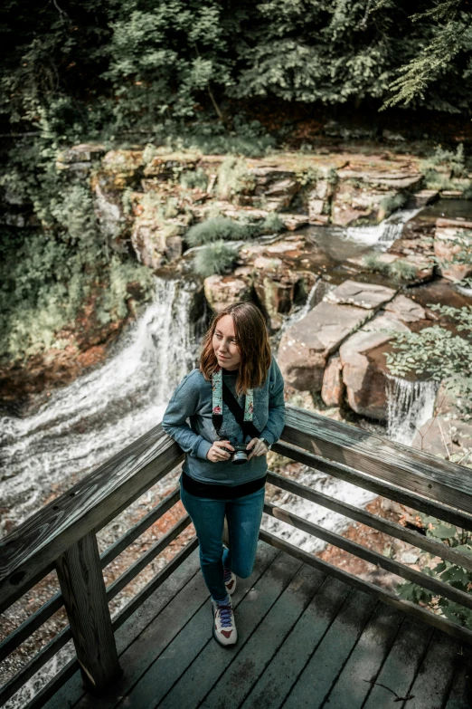 a girl standing on a bridge near a waterfall