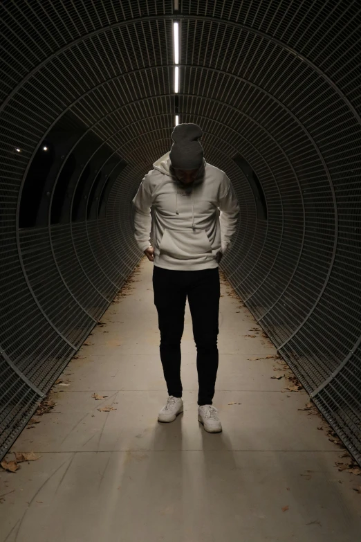 a person wearing a white sweatshirt and black pants walks through a tunnel