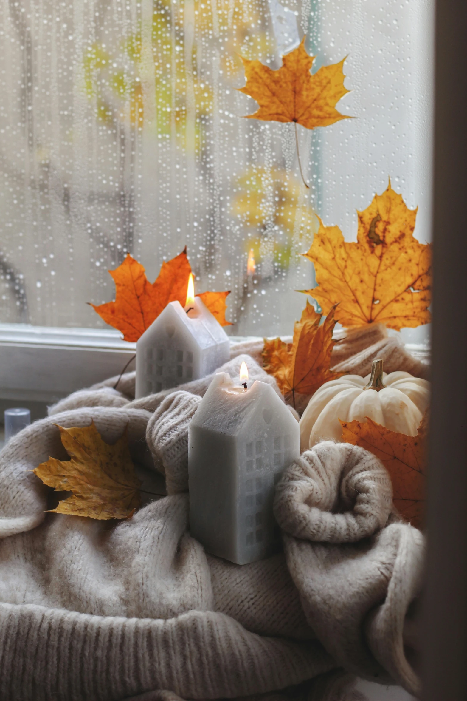 some candles sit on top of a blanket with autumn leaves outside of it