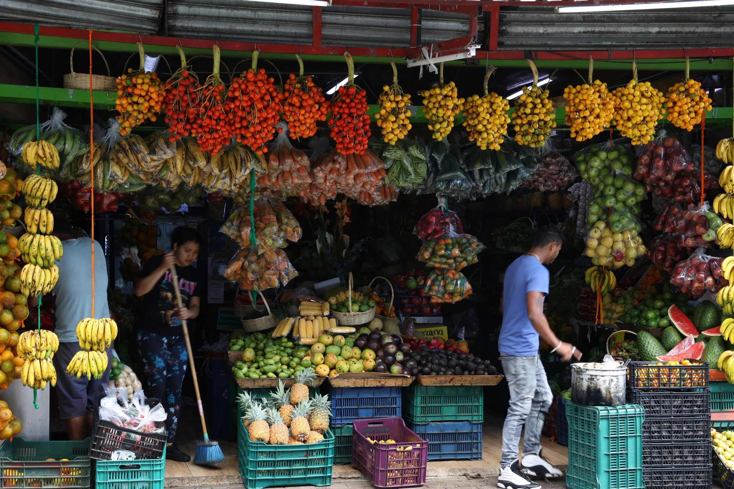 people standing in front of a market filled with bananas and other fruits