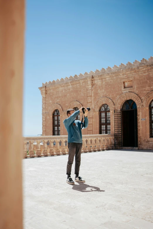 man taking a picture on his cell phone in front of a large brick building