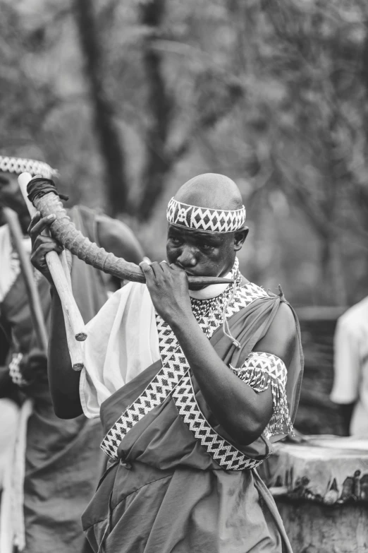 a man wearing a traditional outfit standing with one hand on a stick