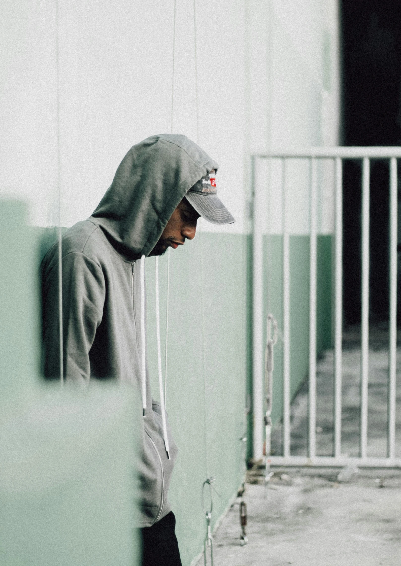 a man in a gray sweatshirt and hat leaning on a green wall